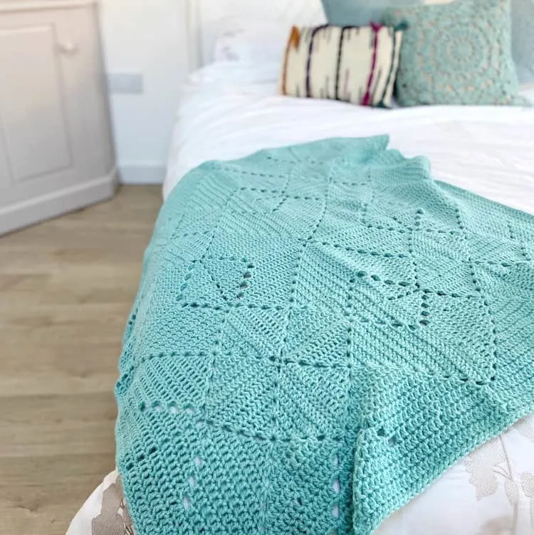 teal coloured crochet granny blanket laid on bed with white sheets