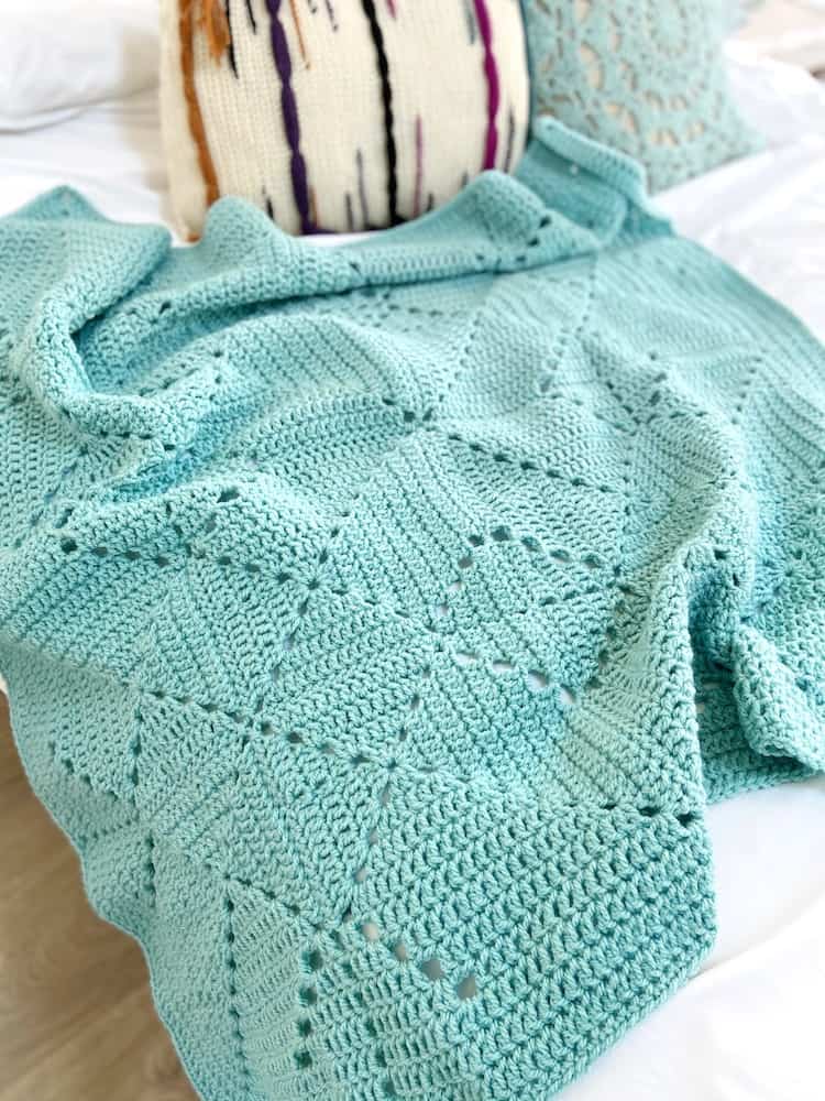 Pale teal crochet blanket on bed with pillows.