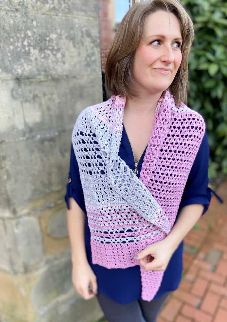 woman looking sideways wearing pink and grey lace crochet shawl wrapped loosely around shoulders