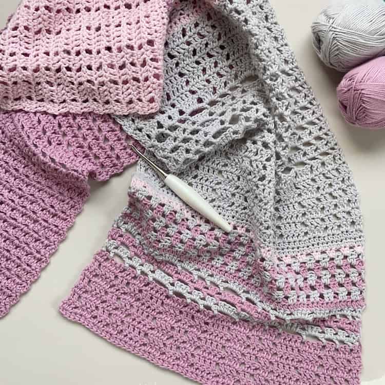 flatlay image of pink and grey summer lace crochet shawl with crochet hook and yarn