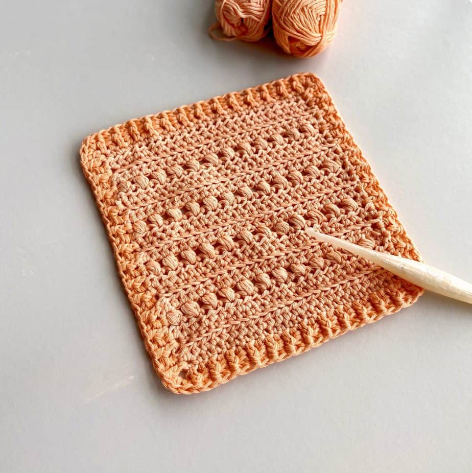crochet puff stitch square with ribbed border on table with crochet hook and peach yarn.