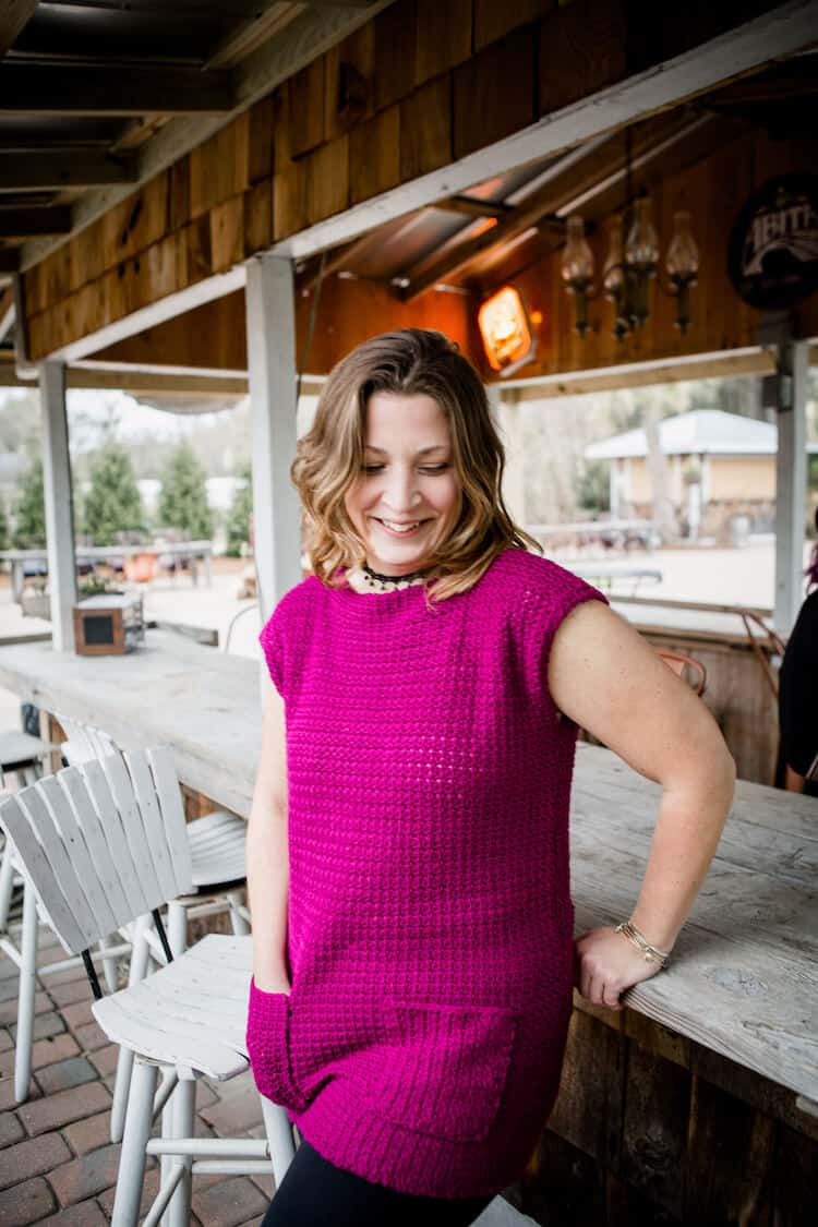 woman looking down, leaning on bar wearing bright pink crochet dress with pockets