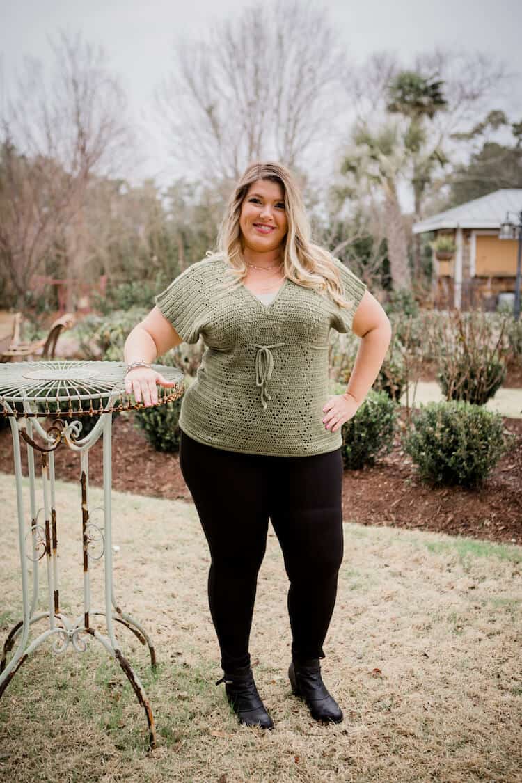 woman standing in garden leaning on table wearing green filet crochet top with under bust tie