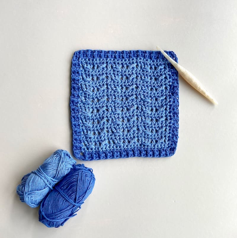 light and dark blue crochet cable stitch square with white crochet hook