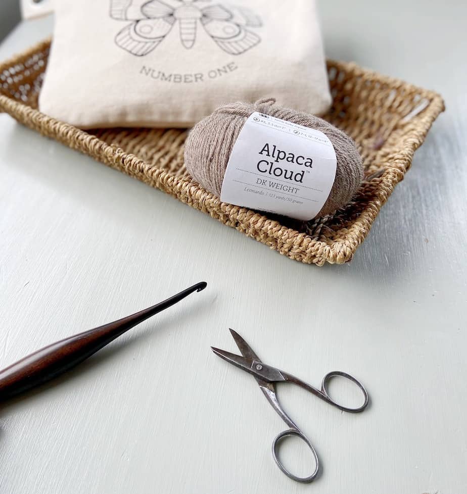 image of alpaca cloud double knit yarn in wicker tray with scissors and crochet hook on desk in front