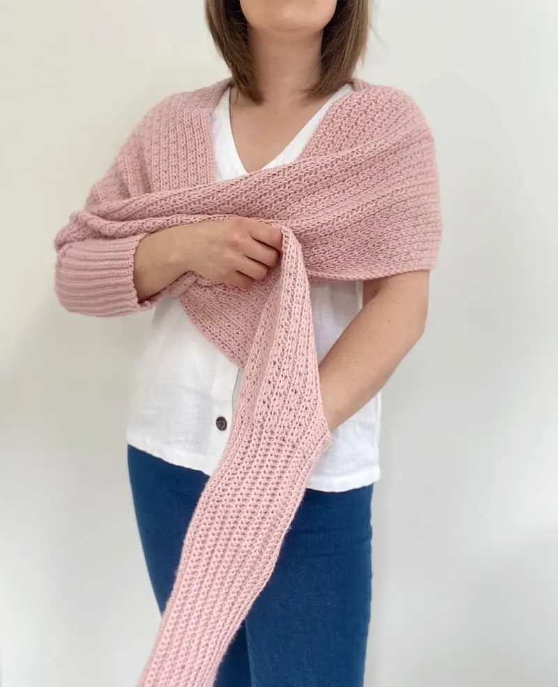 woman putting arm through sleeve of pink scarf with sleeves crochet pattern