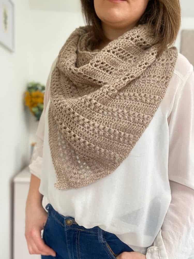 Upper body of woman wearing beige crochet shawl.