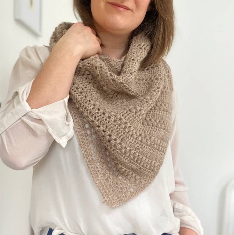 woman in white shirt with a textured lightweight crochet shawl around neck, holding it with one hand at her shoulder.