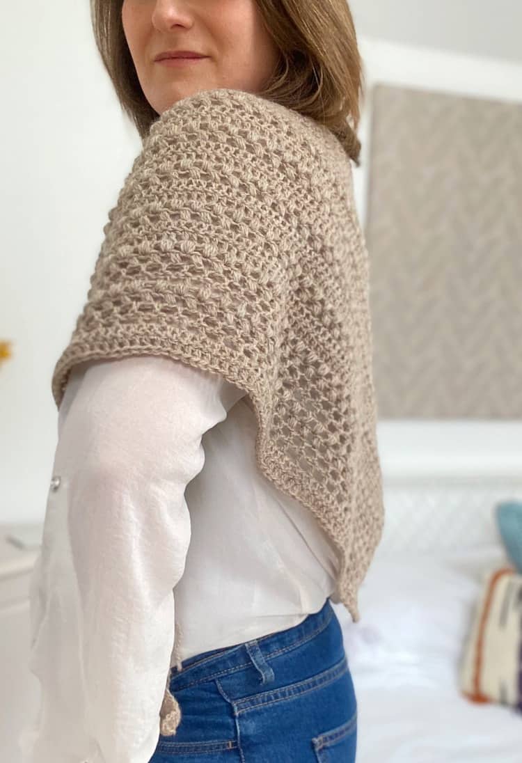 woman looking sideways at camera wearing a textured triangle crochet shawl across her back and shoulders