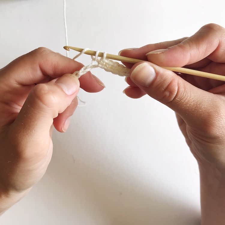 Two hands holding crochet needle and white yarn.