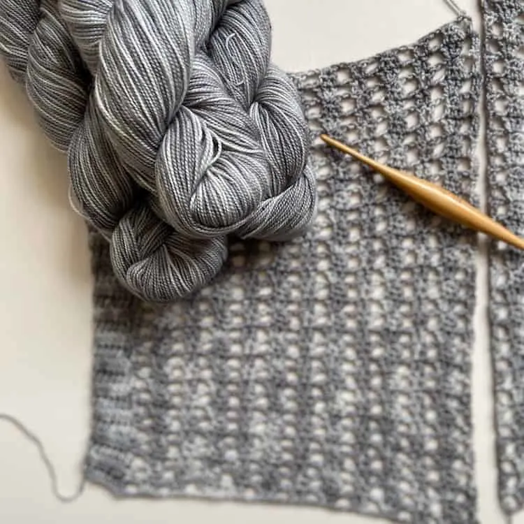 grey fingering weight yarn in hanks laid on crochet lace panel with wooden crochet hook