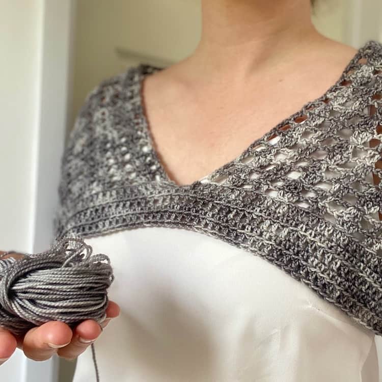 woman wearing a partially made v neck crochet top holding a ball of yarn