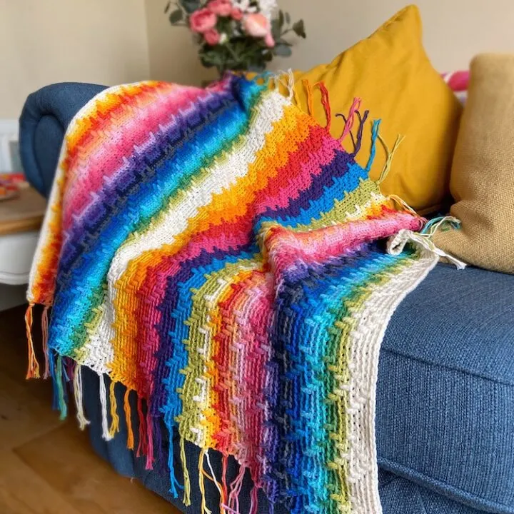 rainbow overlay mosaic crochet blanket on a blue sofa