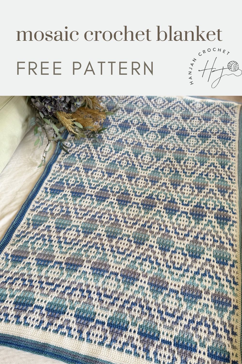 A blue and white mosaic crochet blanket with a striking geometric pattern is displayed on a light surface beside dried flowers. Text reads: "mosaic crochet blanket FREE PATTERN." Perfect for your next mosaic crochet project.