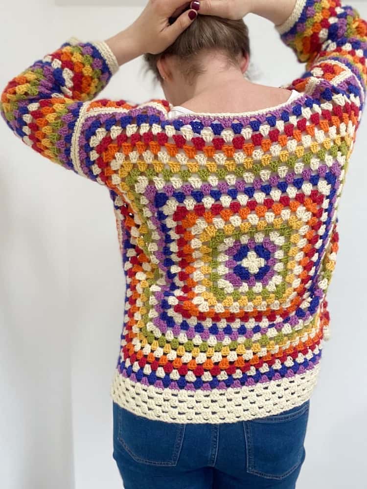 Back view of person wearing crochet rainbow granny square sweater holding hair up so you can see the back.