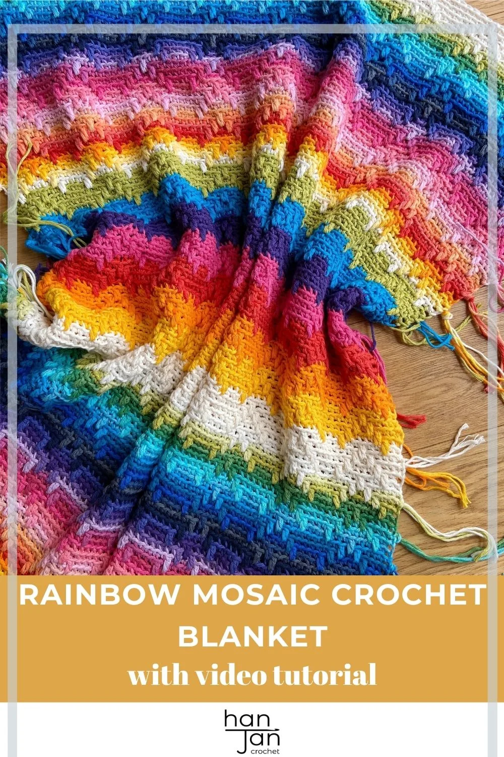 rainbow crochet blanket using overlay mosaic crochet technique with tassels laid on wooden floor