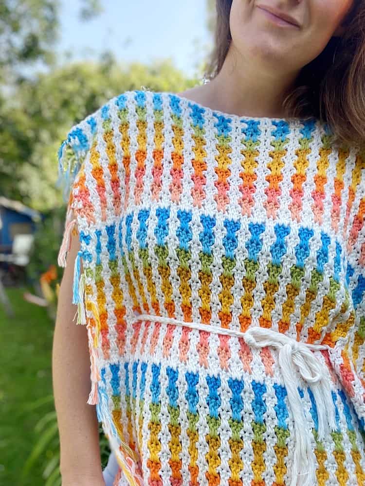 woman wearing colourful crochet poncho with white braided belt around waist