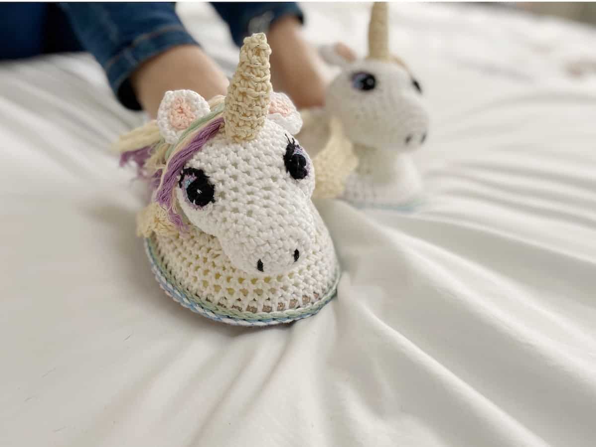 close up of amigurumi unicorn crochet slippers on a someone wearing blue jeans