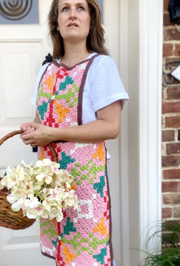 Woman wearing crochet apron and holding basket of flowers.