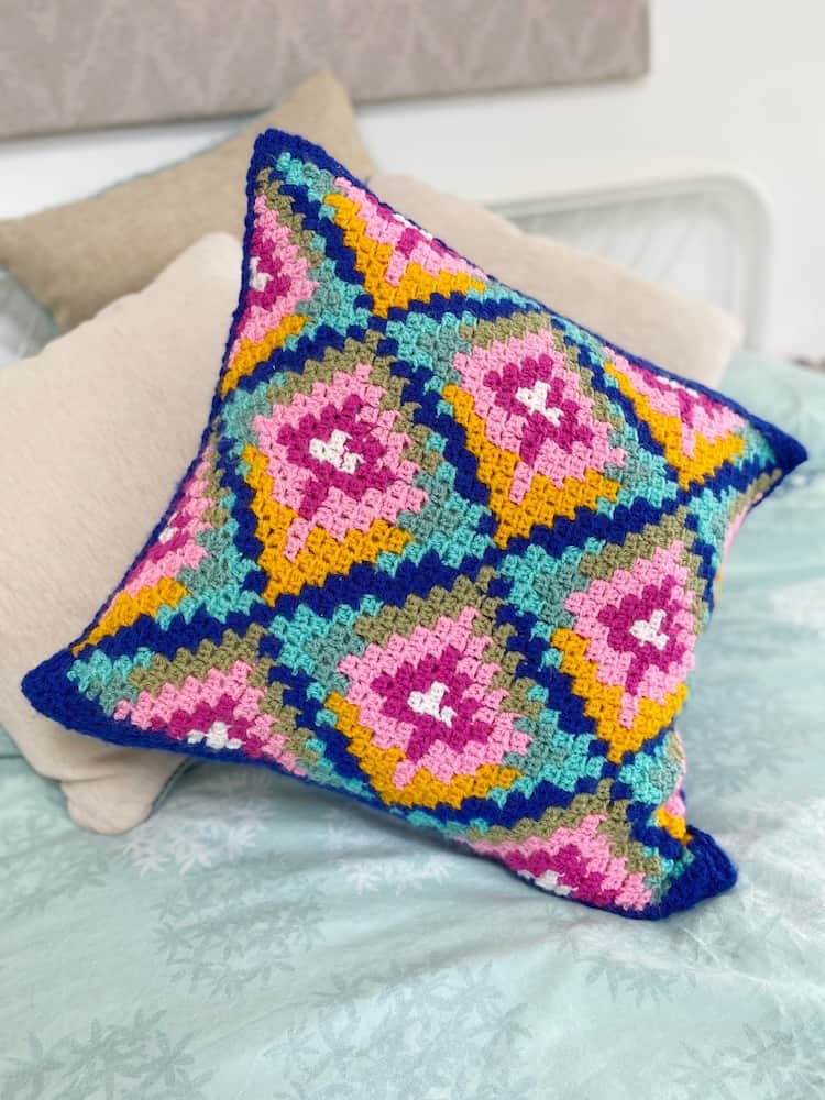 Bargello inspired colourful c2c crochet pillow on bed.