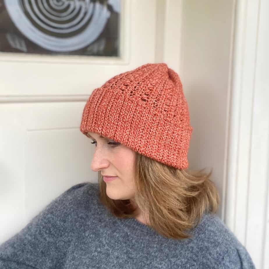 woman leaning against cream door wearing slouchy crochet hat with wavy hair and grey sweater