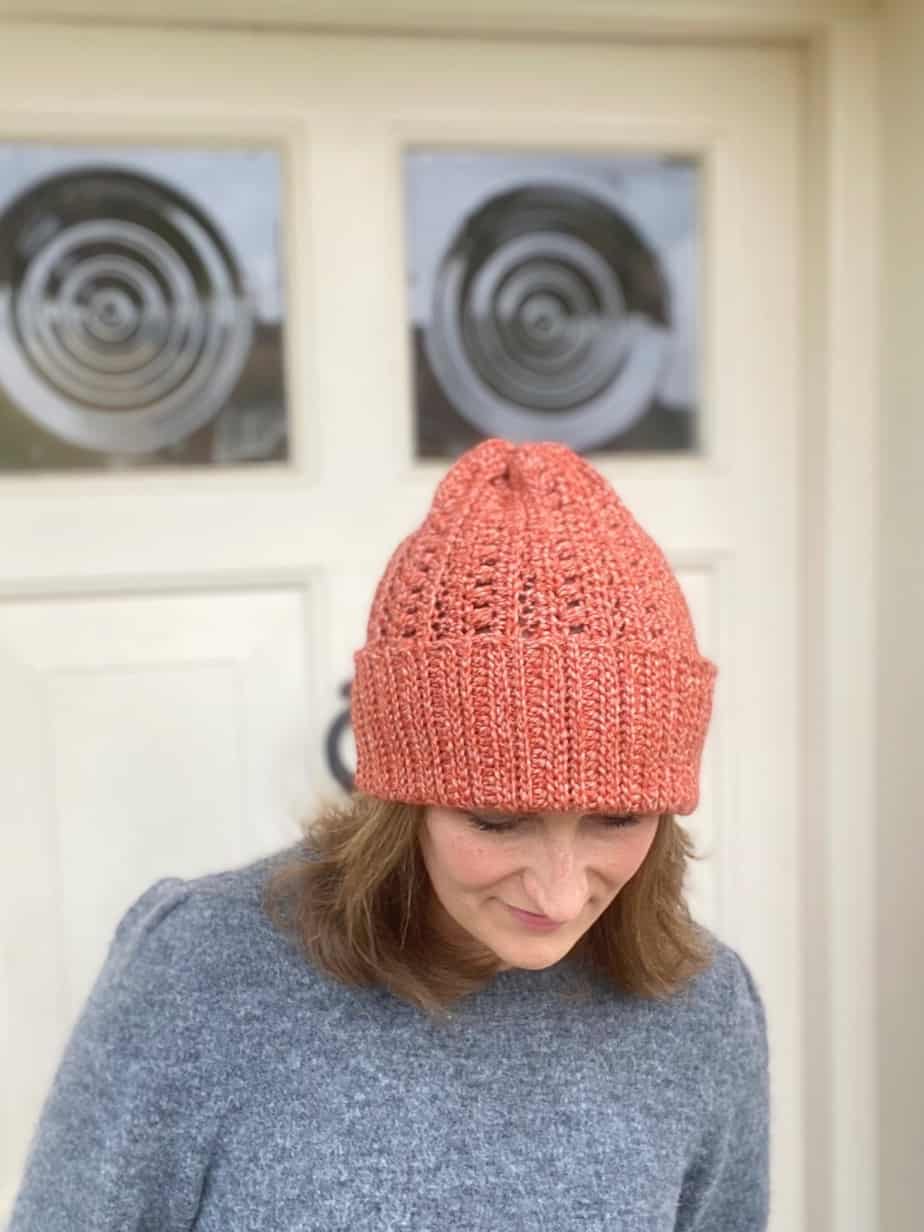 woman standing in front of cream door wearing grey sweater and pumpkin colour slouchy crochet beanie