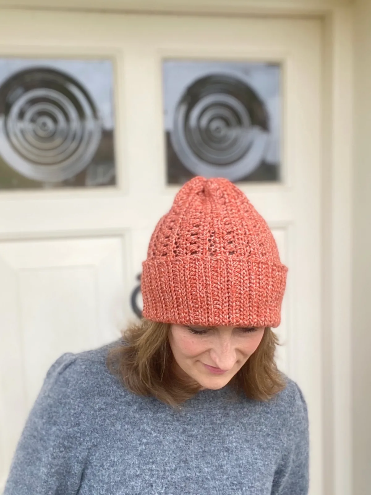woman standing in front of cream door wearing grey sweater and pumpkin colour slouchy crochet beanie