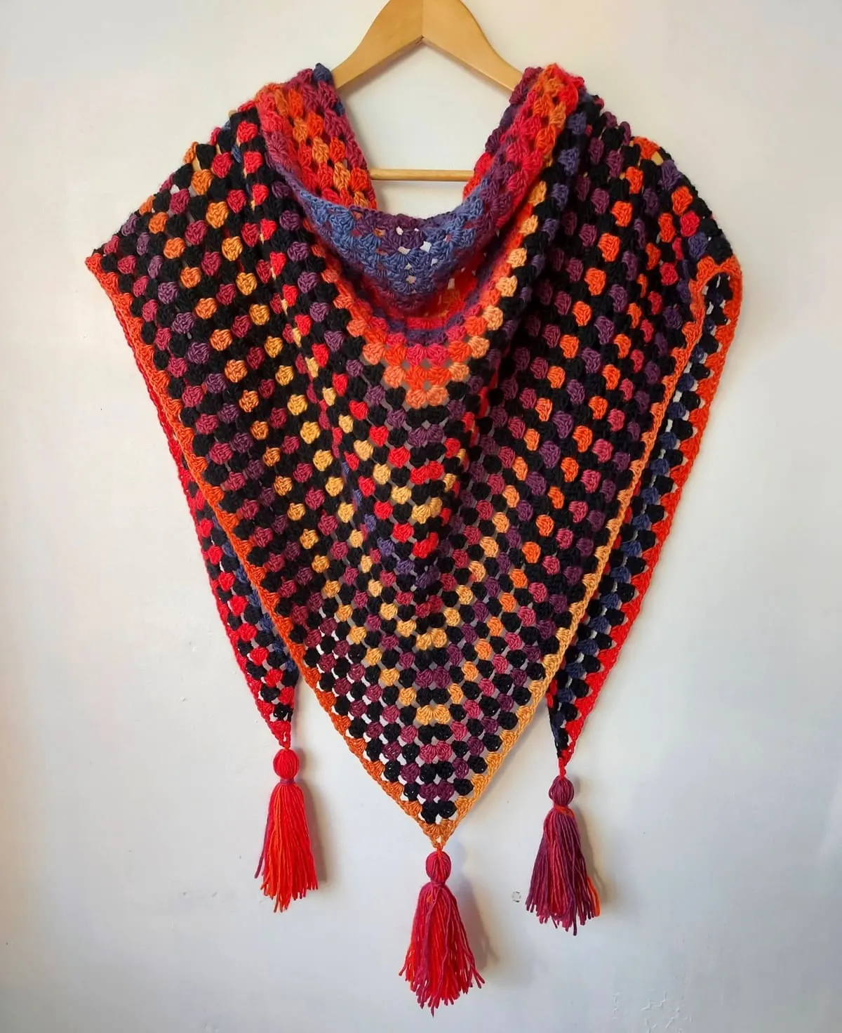 Granny stitch triangle shawl with tassels in bright orange, yellow and black colours.