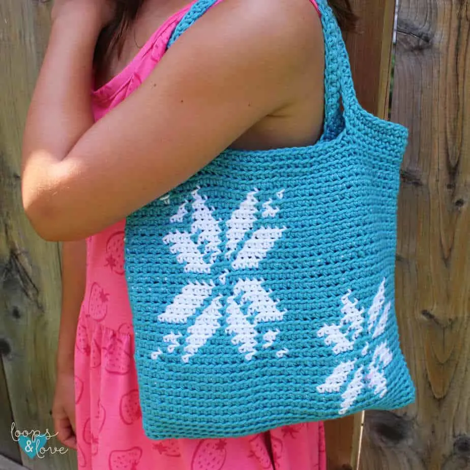 Woman's upper body holding a blue crocheted bag with snowflake design over her shoulder.
