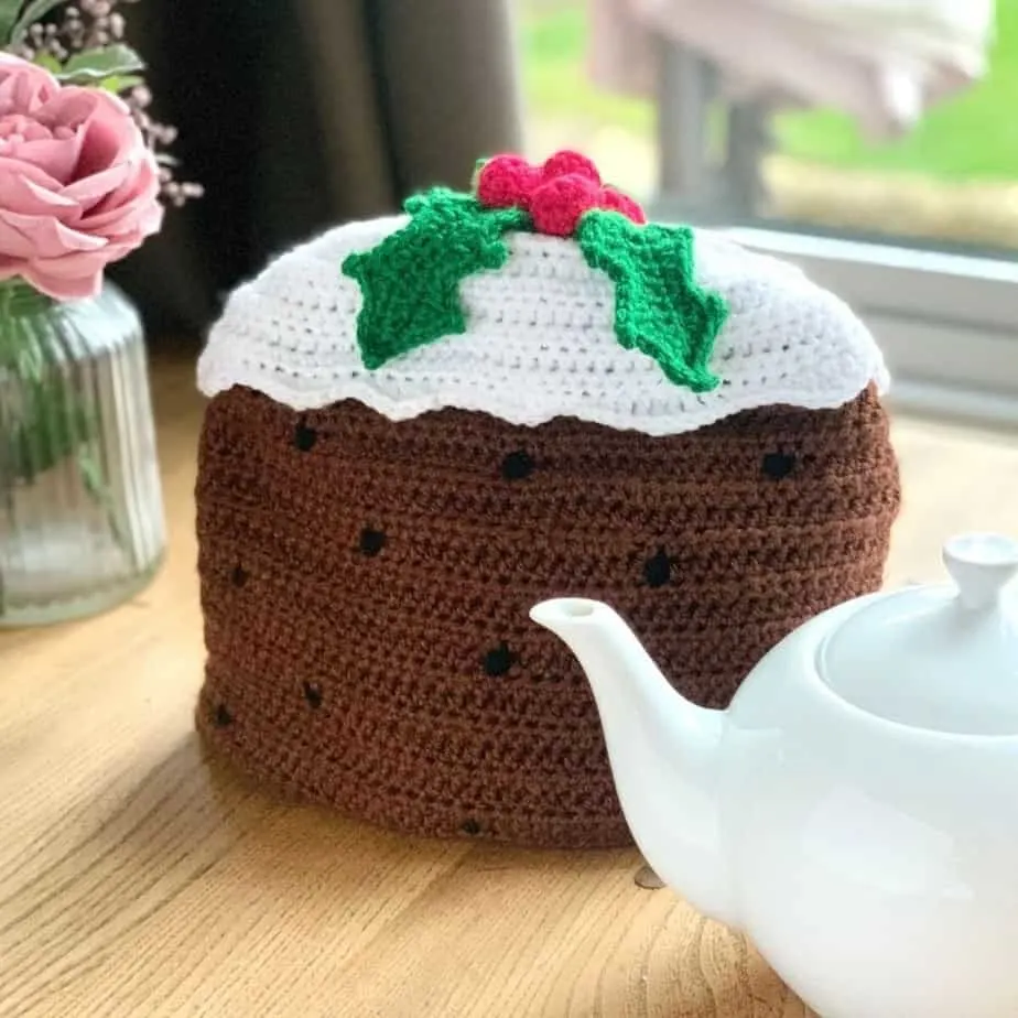 Crocheted Christmas pudding tea cosy next to white tea pot.