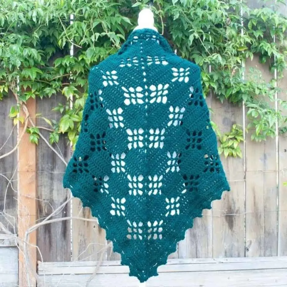 Dark green lacy shawl displayed over dress form.