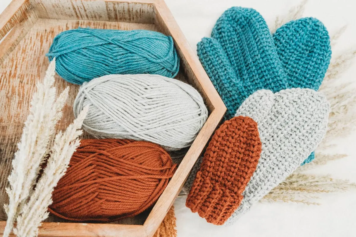 Three pairs of mittens next to three skeins of yarn.