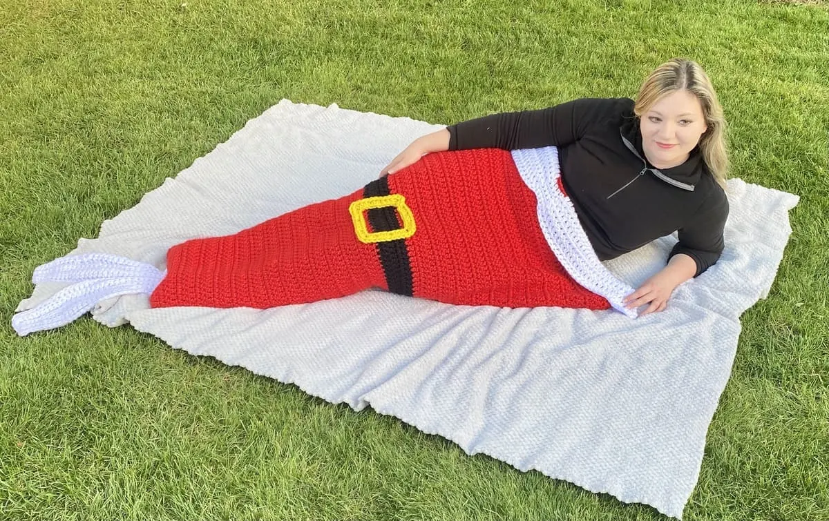Woman lying on a blanket on the grass, wearing Santa mermaid tail blanket.