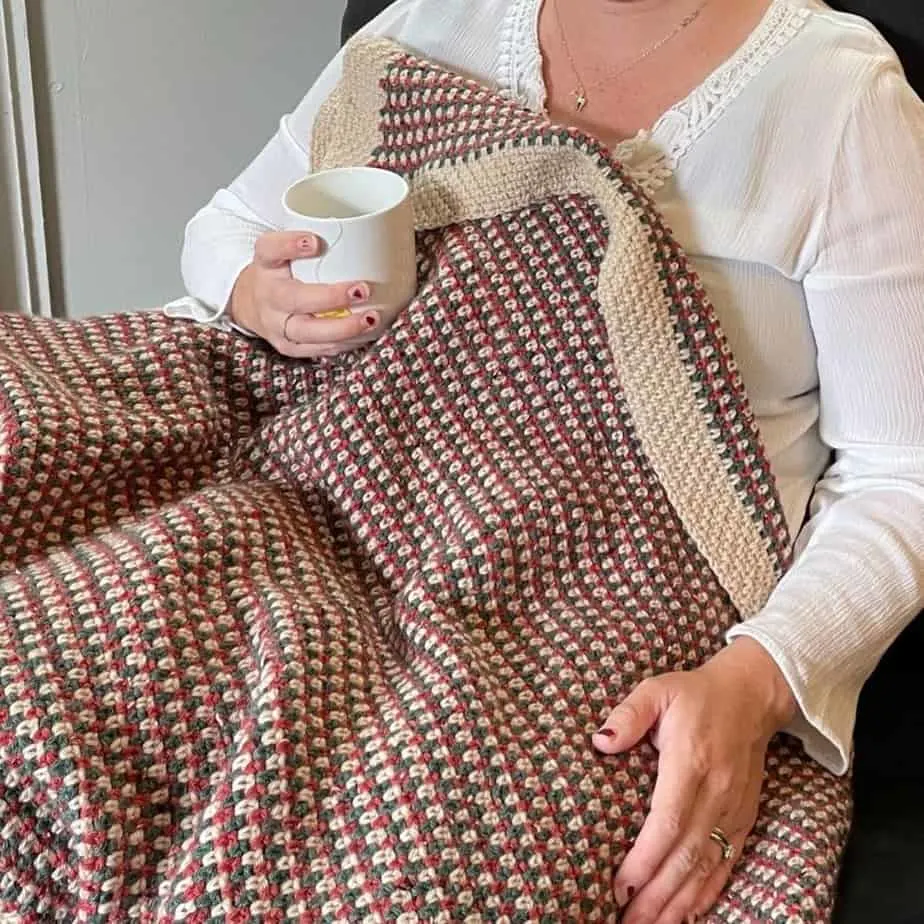 Woman sitting in a chair holding a teacup with red and green lapghan over her lap.