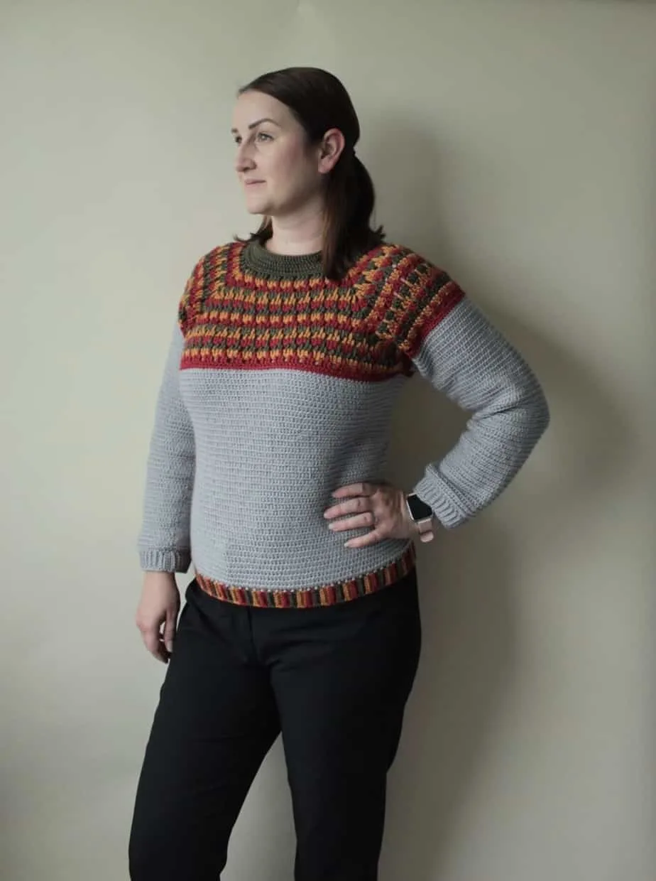 Woman wearing gray and multi-colored crocheted sweater.
