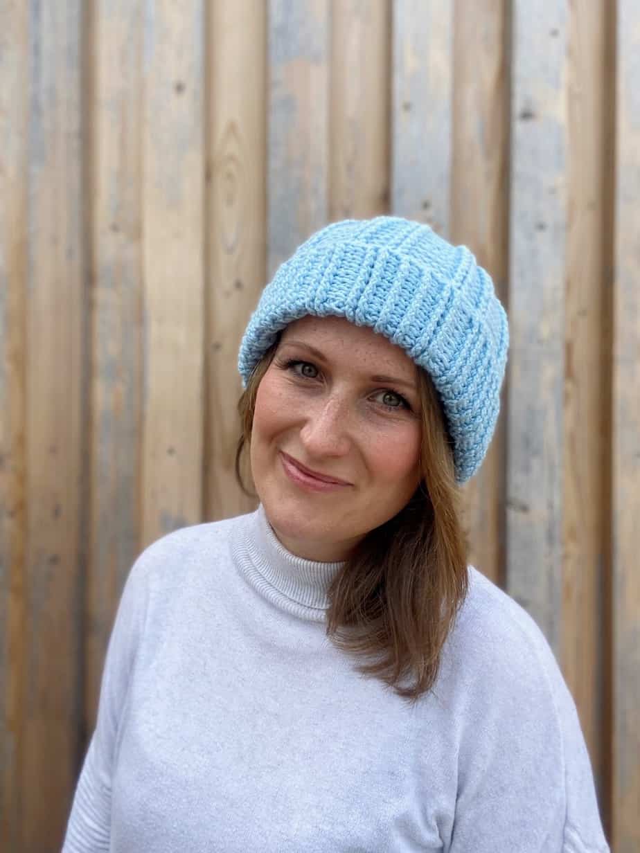 woman smiling and wearing a blue crochet bobble hat with texture detail and turned back brim