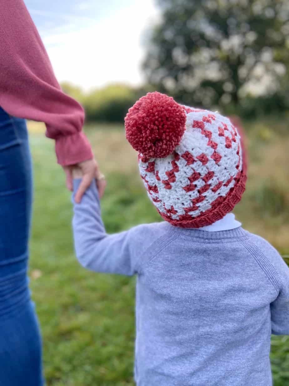 picture of child holding adults hand walking away wearing winter crochet hat with pom pom