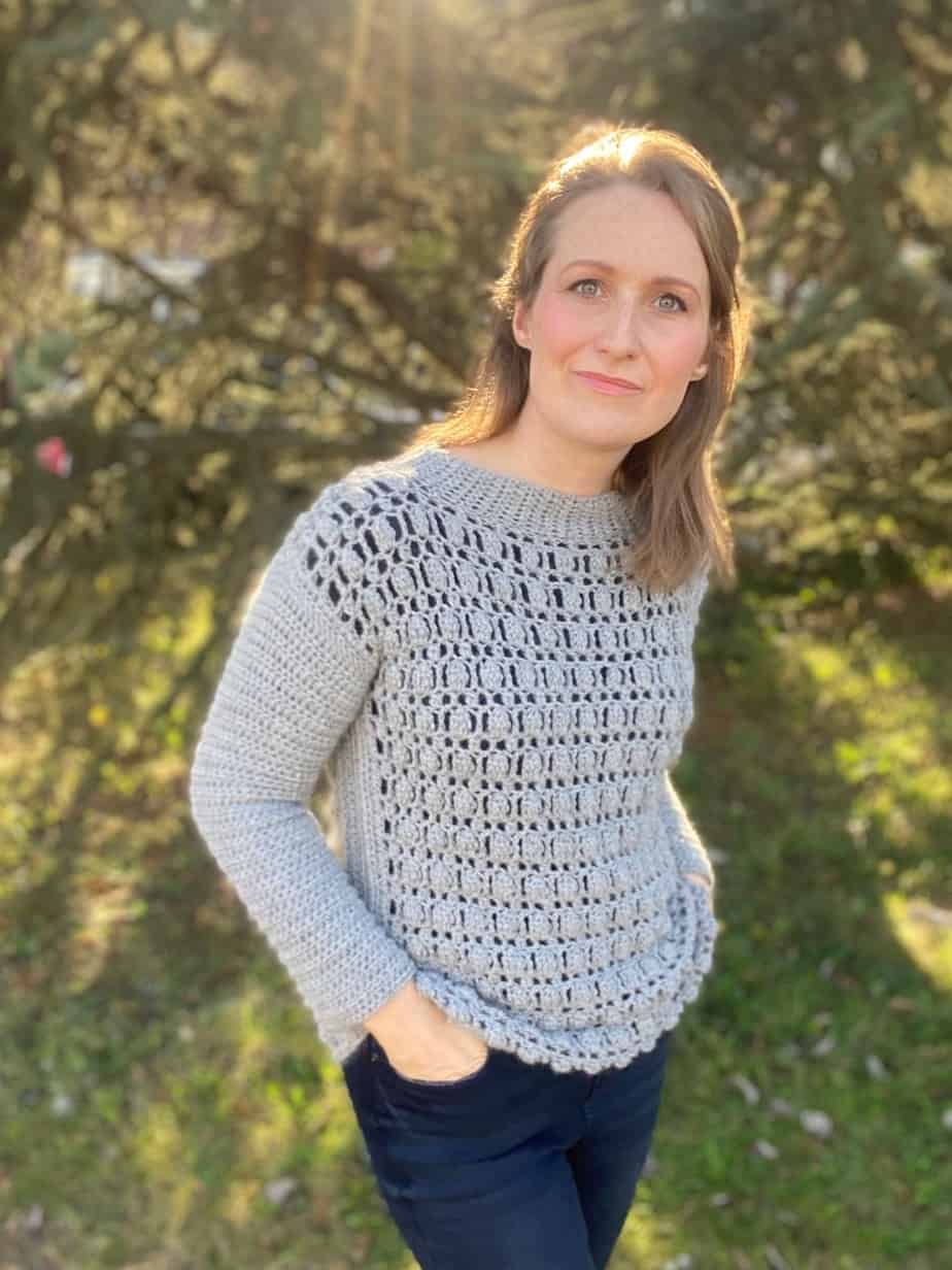 woman looking at camera with hands in pockets wearing crochet sweater with cluster stitch detail