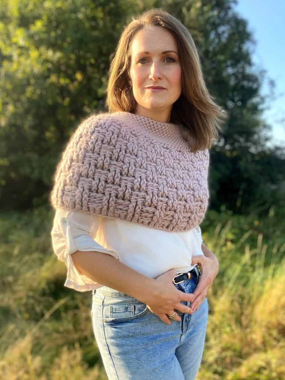 woman in field wearing jeans, white shirt and chunky crochet cape over shoulders
