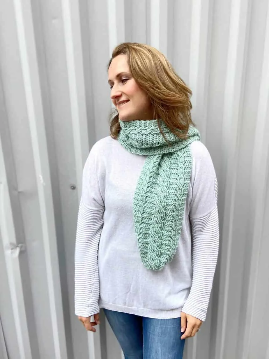free cable crochet scarf pattern worn by woman against an industrial background
