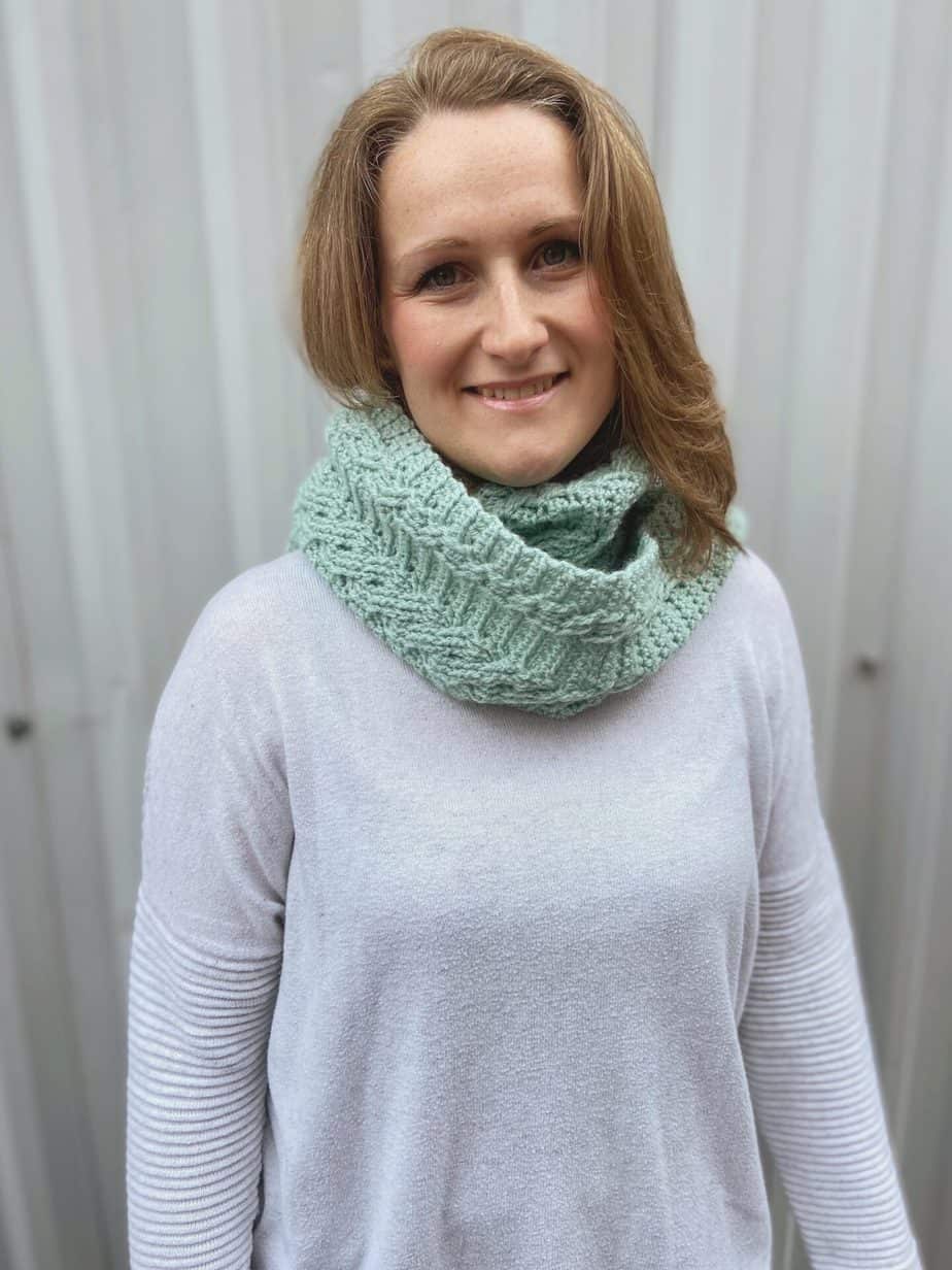 free cable crochet scarf pattern shown wrapped around a neck as a cowl
