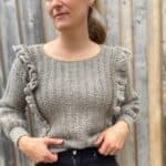 woman wearing grey ruffle stitch crochet sweater tucked into black jeans