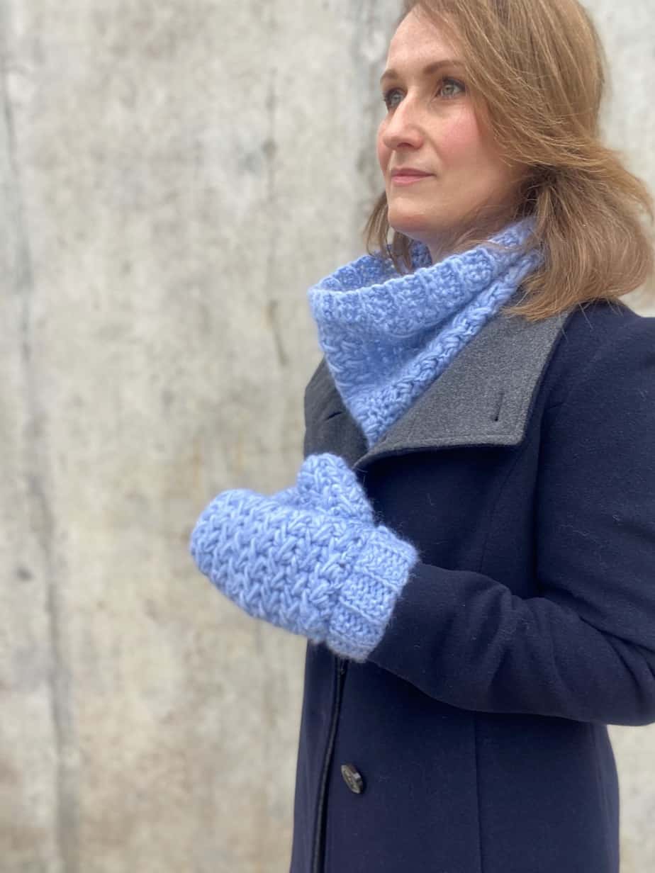 Woman wearing navy wool coat and light blue feather stitch full finger crochet mittens and cowl.