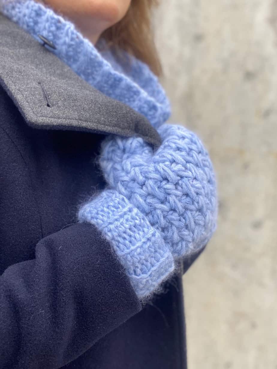 Person wearing soft crochet mittens and cowl holding onto collar of navy wool coat.