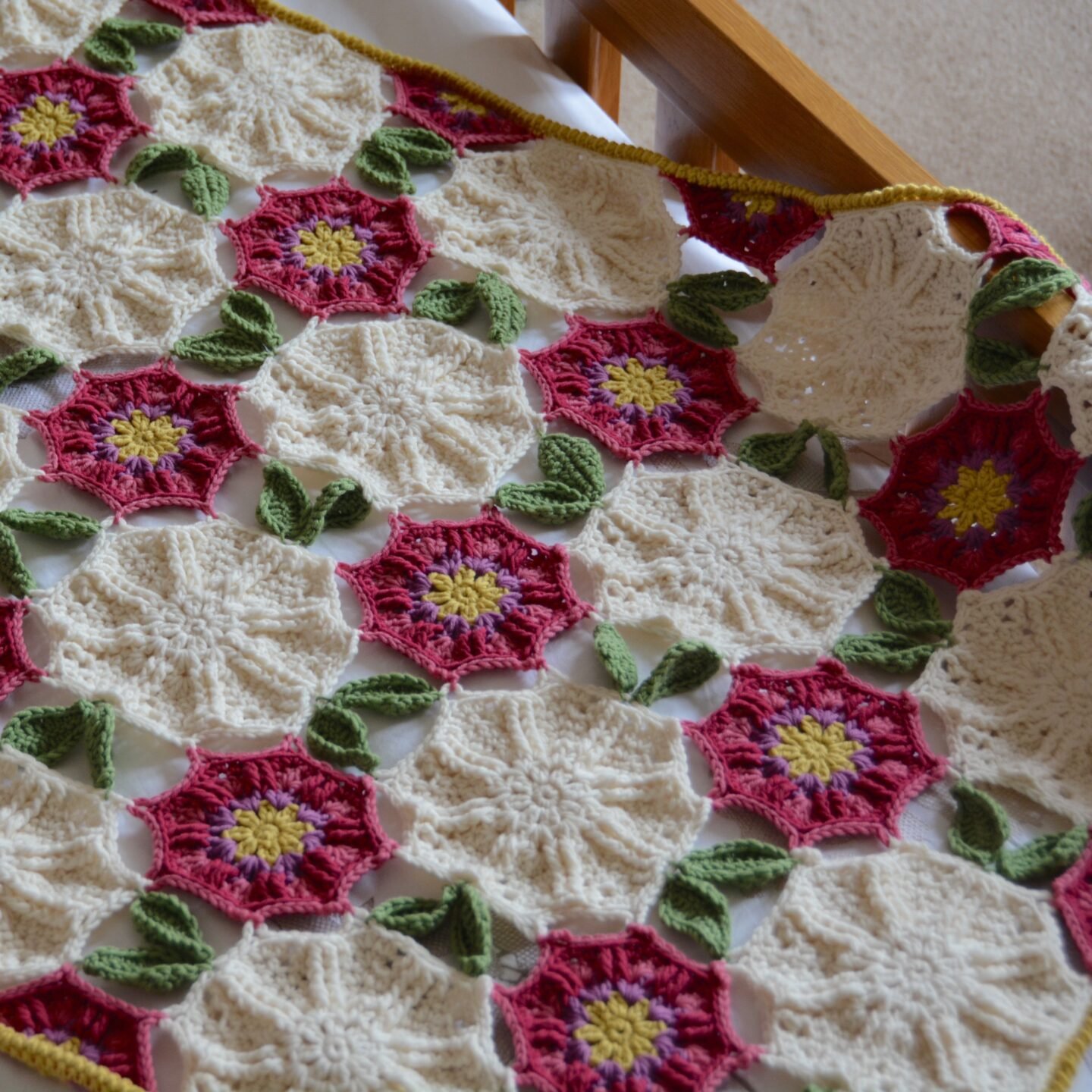 crochet flower blanket laid over wooden bed