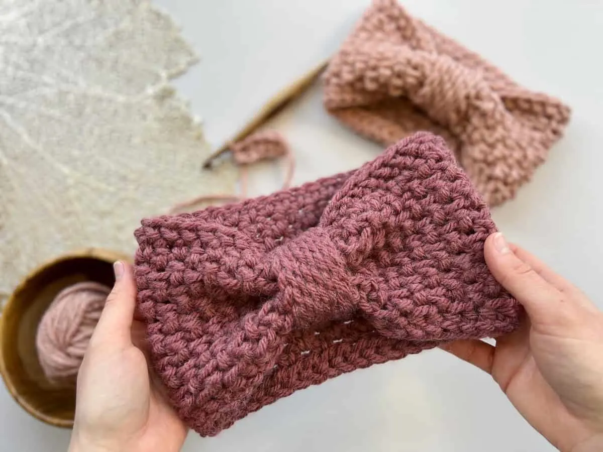 hands holding up a free crochet headband pattern that looks like a bow