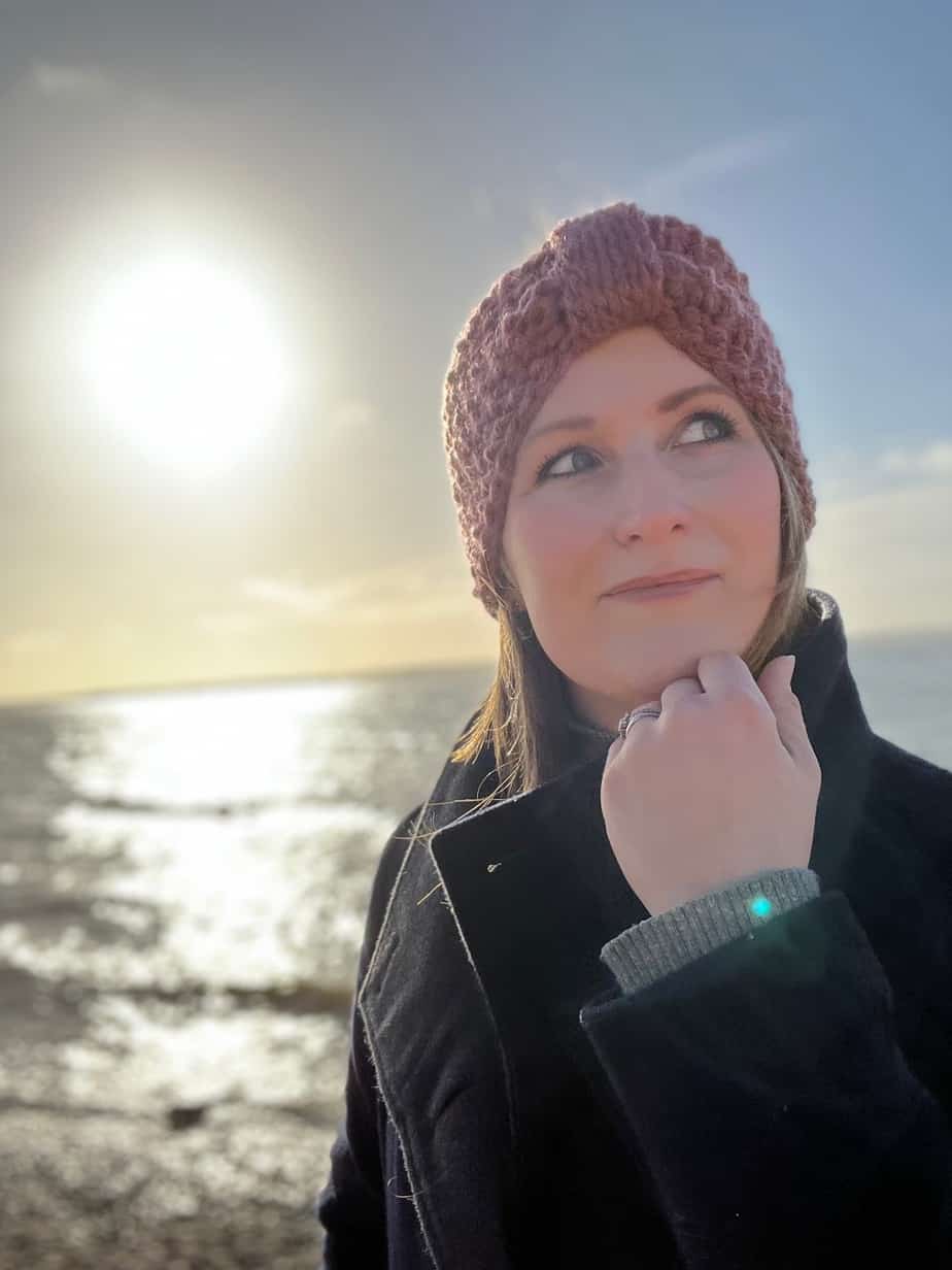 woman at the beach wearing wool coat and free crochet headband pattern in pink