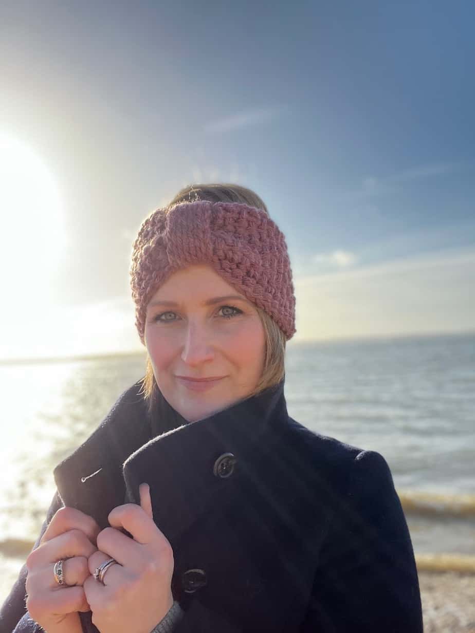woman at the beach wearing chunky crochet headband looking at the camera and holding her coat collar