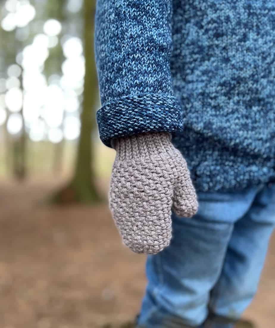 close up of child wearing knitted cardigan and herringbone moss stitch crochet mittens in grey