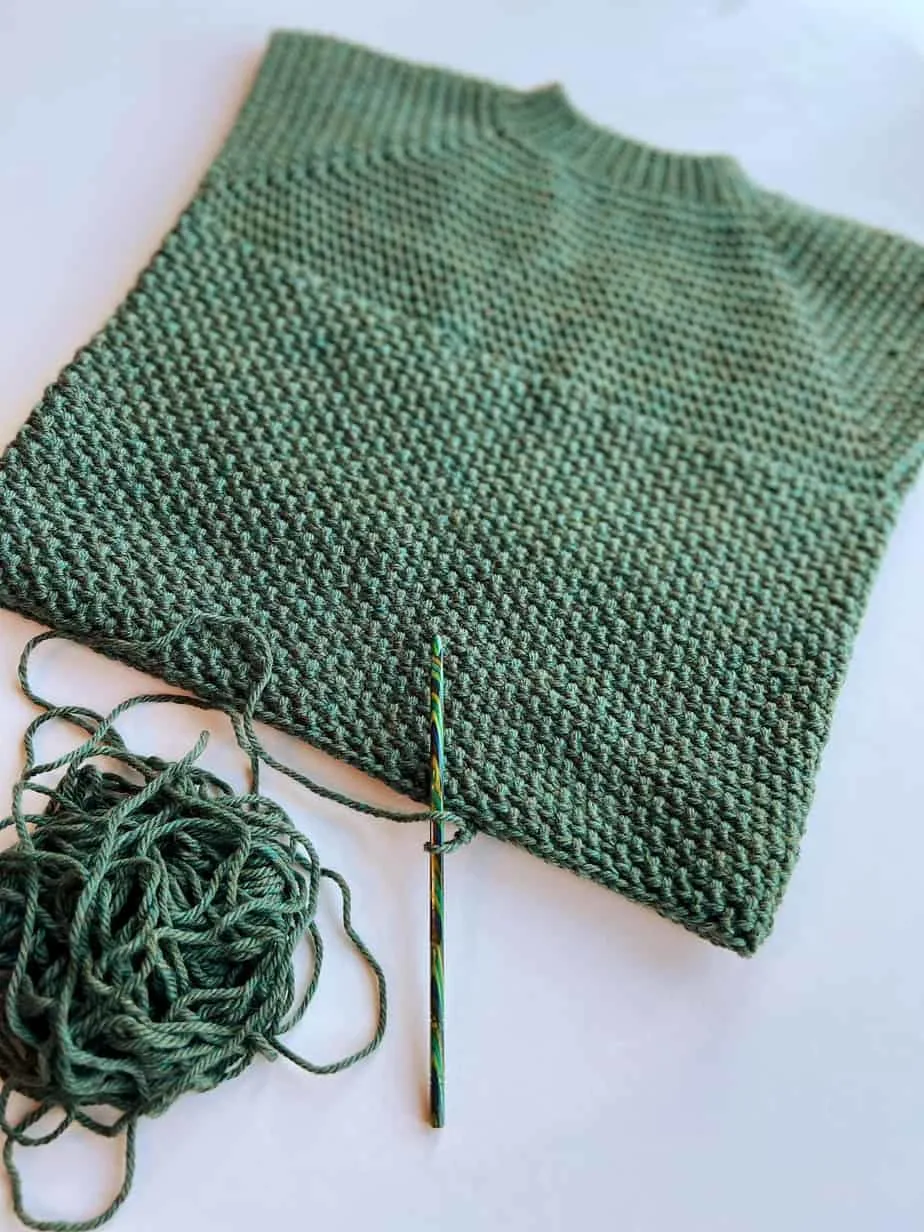 progress image of a green crochet raglan sweater in child size with green crochet hook